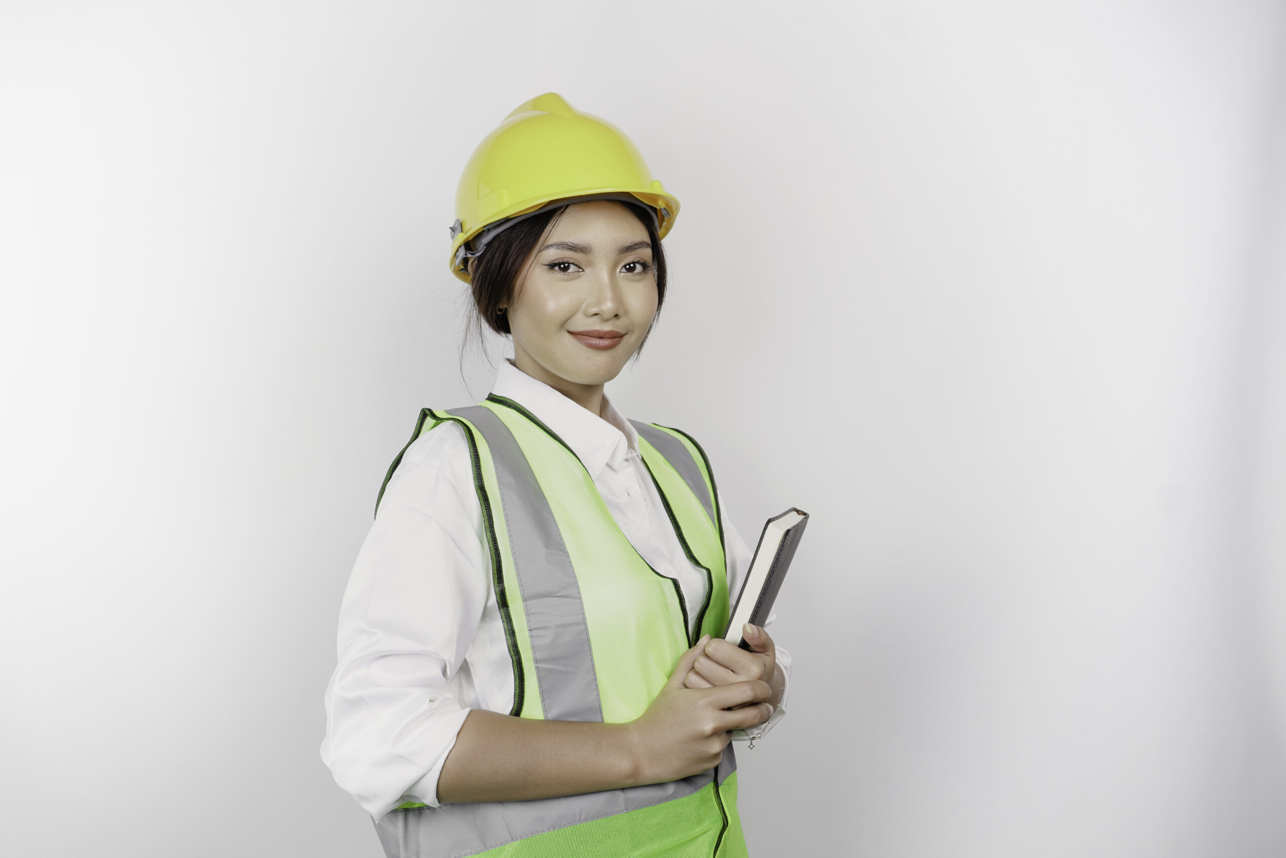 Smiling asian woman labor wearing safety helmet vest holding her book isolated by white background labor s day concept scaled